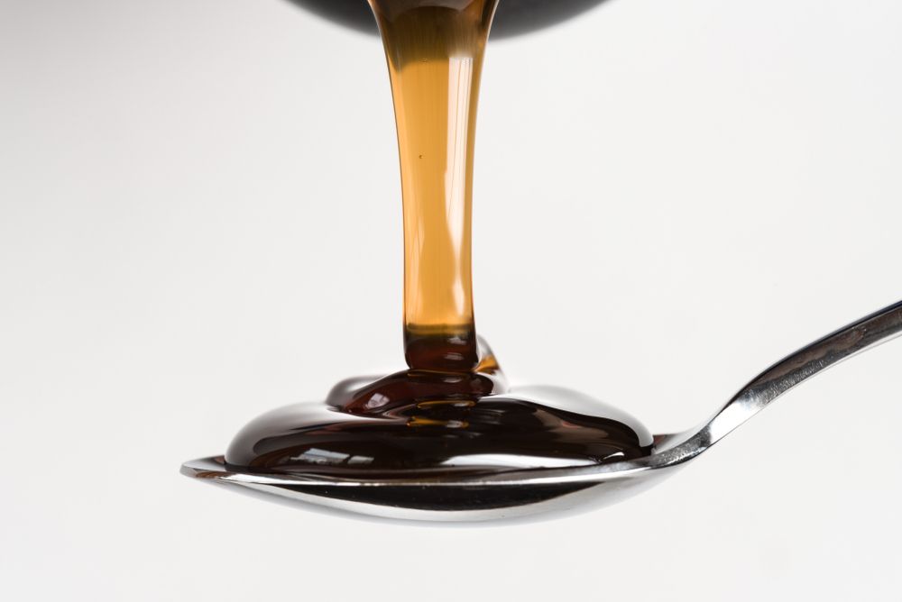 Syrup is being poured into a spoon on a white background