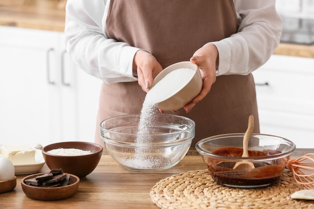 woman pouring sugar into a bowl while baking brownies