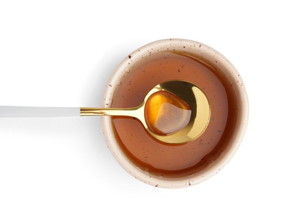 A bowl of maple syrup with a gold spoon in it.