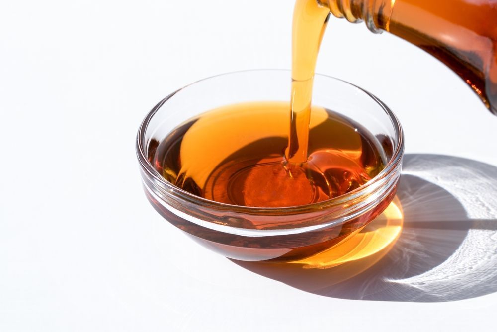 A bottle of syrup is being poured into a glass bowl.