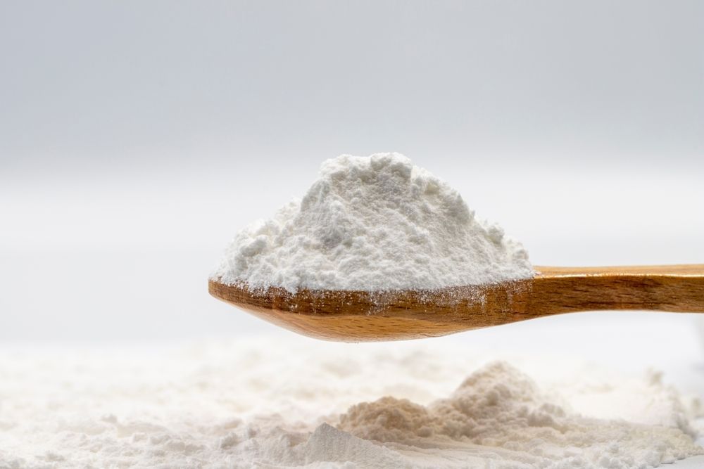 A wooden spoon filled with flour is sitting on top of a pile of flour.