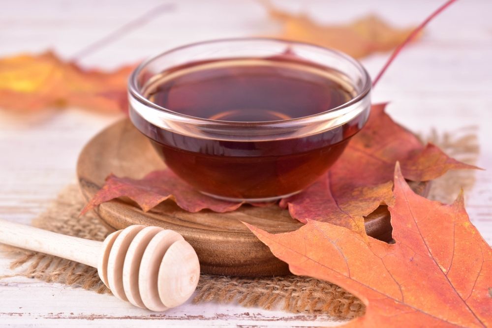 A bowl of maple syrup and a wooden honey dipper on a wooden plate.