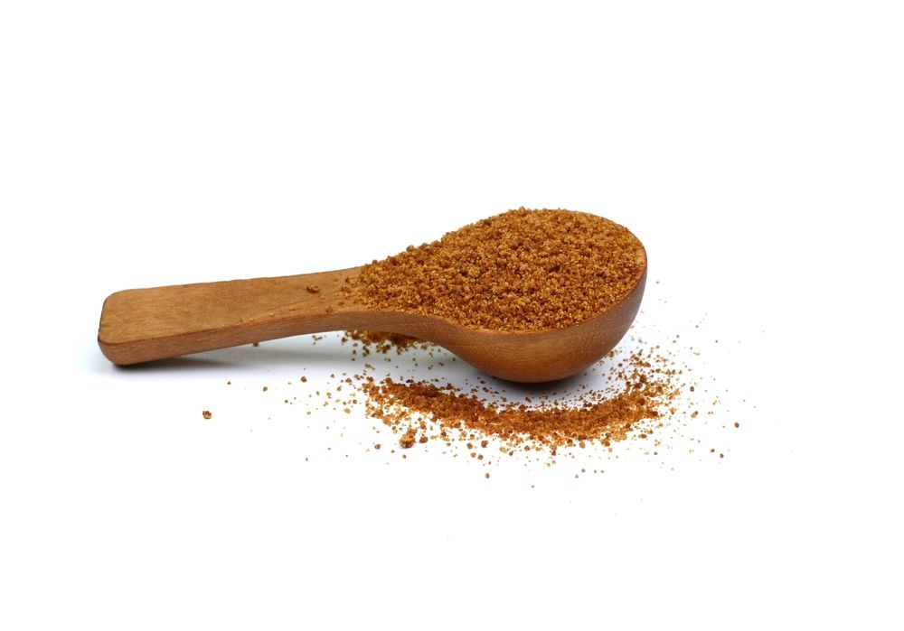 A wooden spoon filled with coconut sugar on a white background.