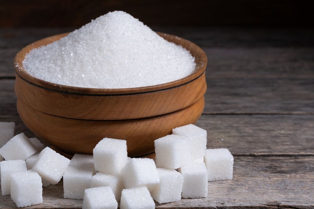 A wooden bowl filled with sugar and sugar cubes on a wooden table.