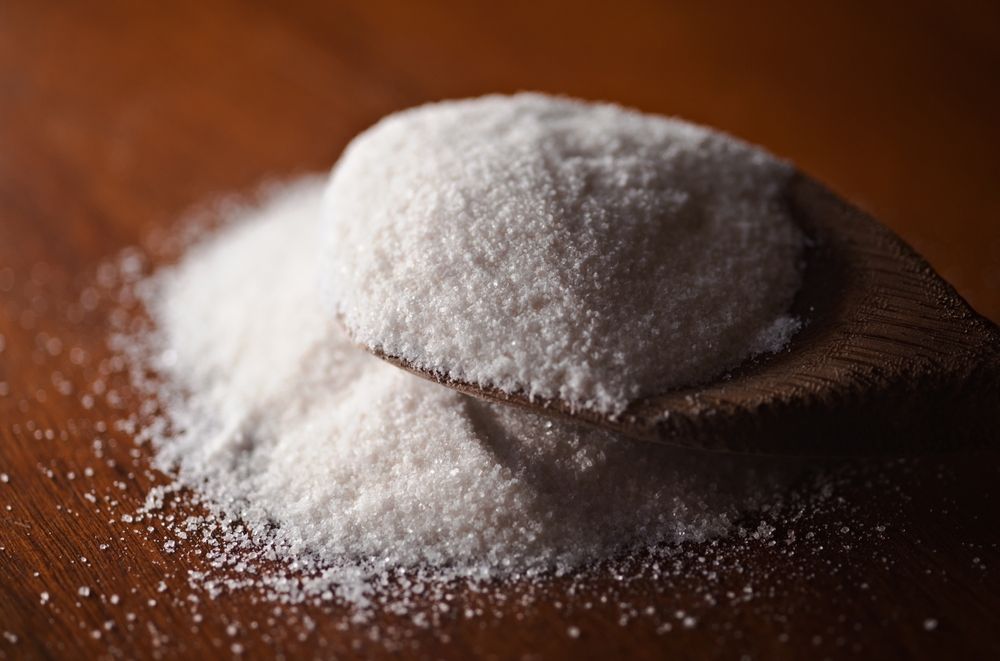 A pile of xylitol on a wooden spoon on a wooden table.