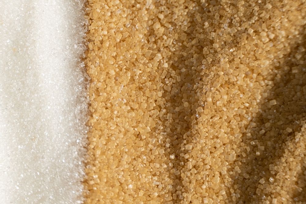 A close up of two piles of sugar , one white and one brown.