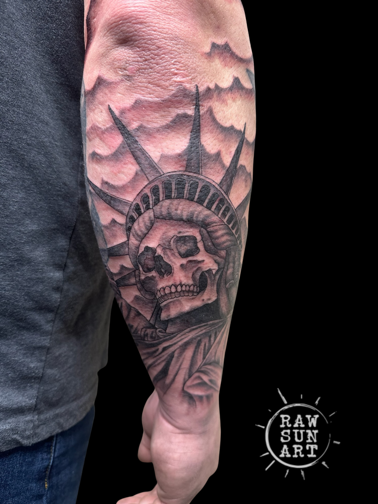 A man has a tattoo of the statue of liberty with a skull on his forearm.
