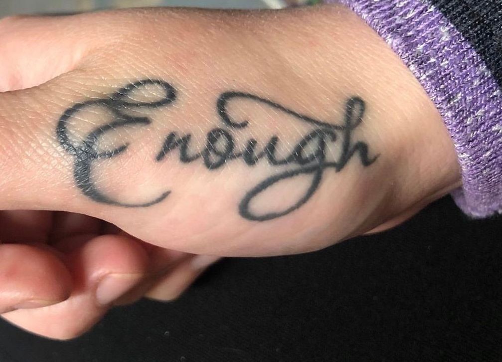 A person has a tattoo on their hand that says enough
