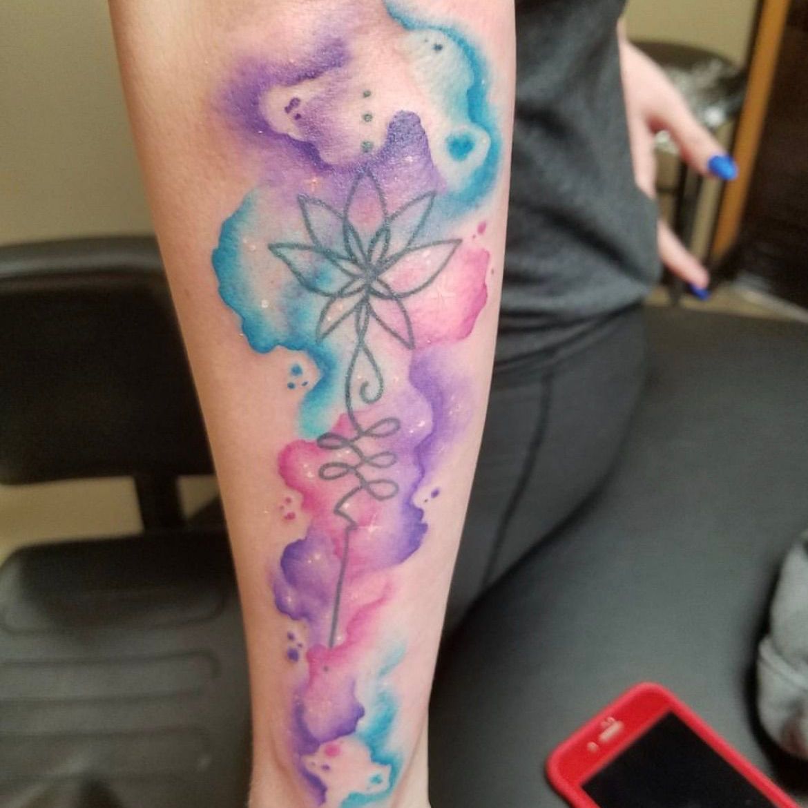 A woman has a watercolor tattoo of a flower on her forearm