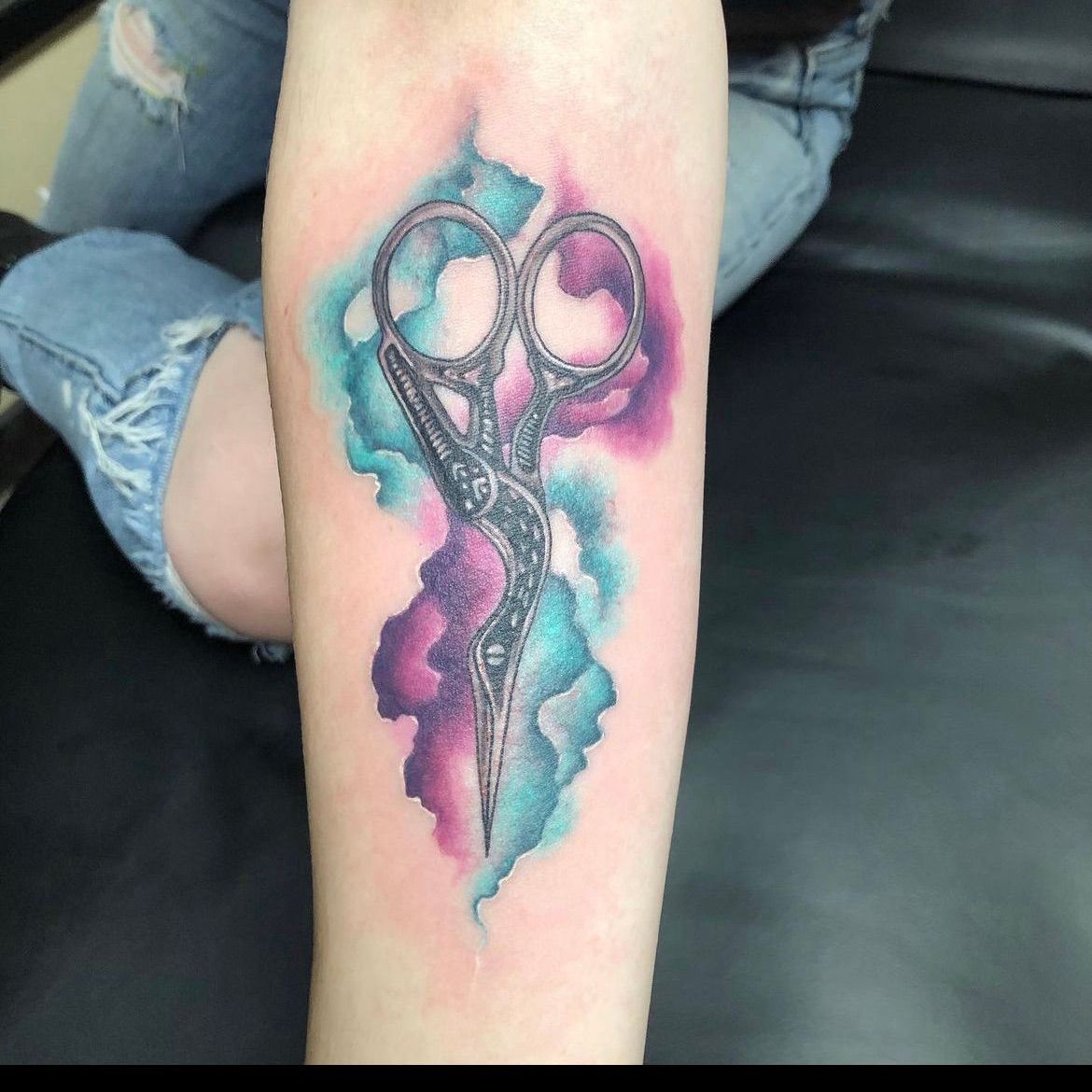 A tattoo of a pair of scissors on a person 's arm