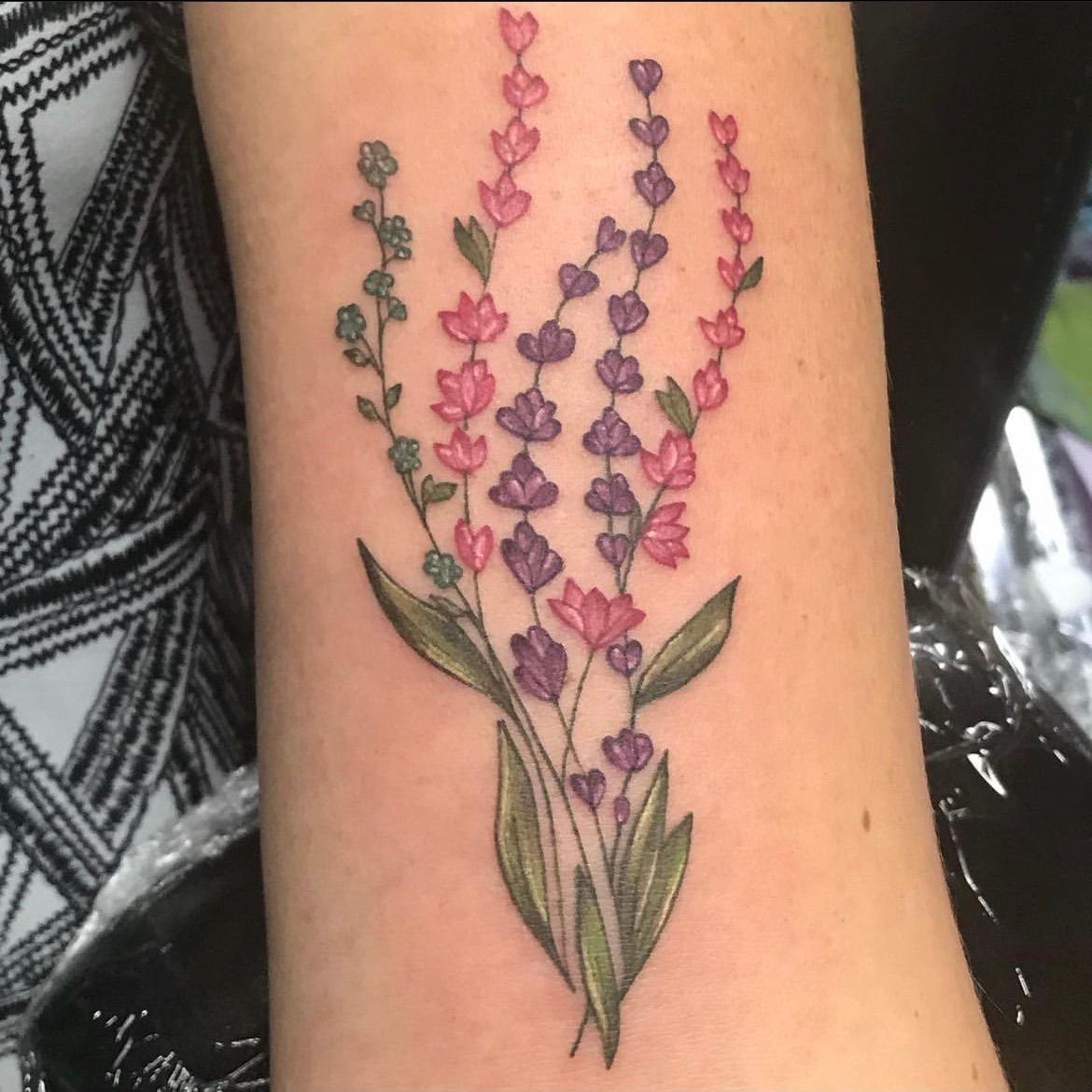 A woman has a tattoo of purple and pink flowers on her arm