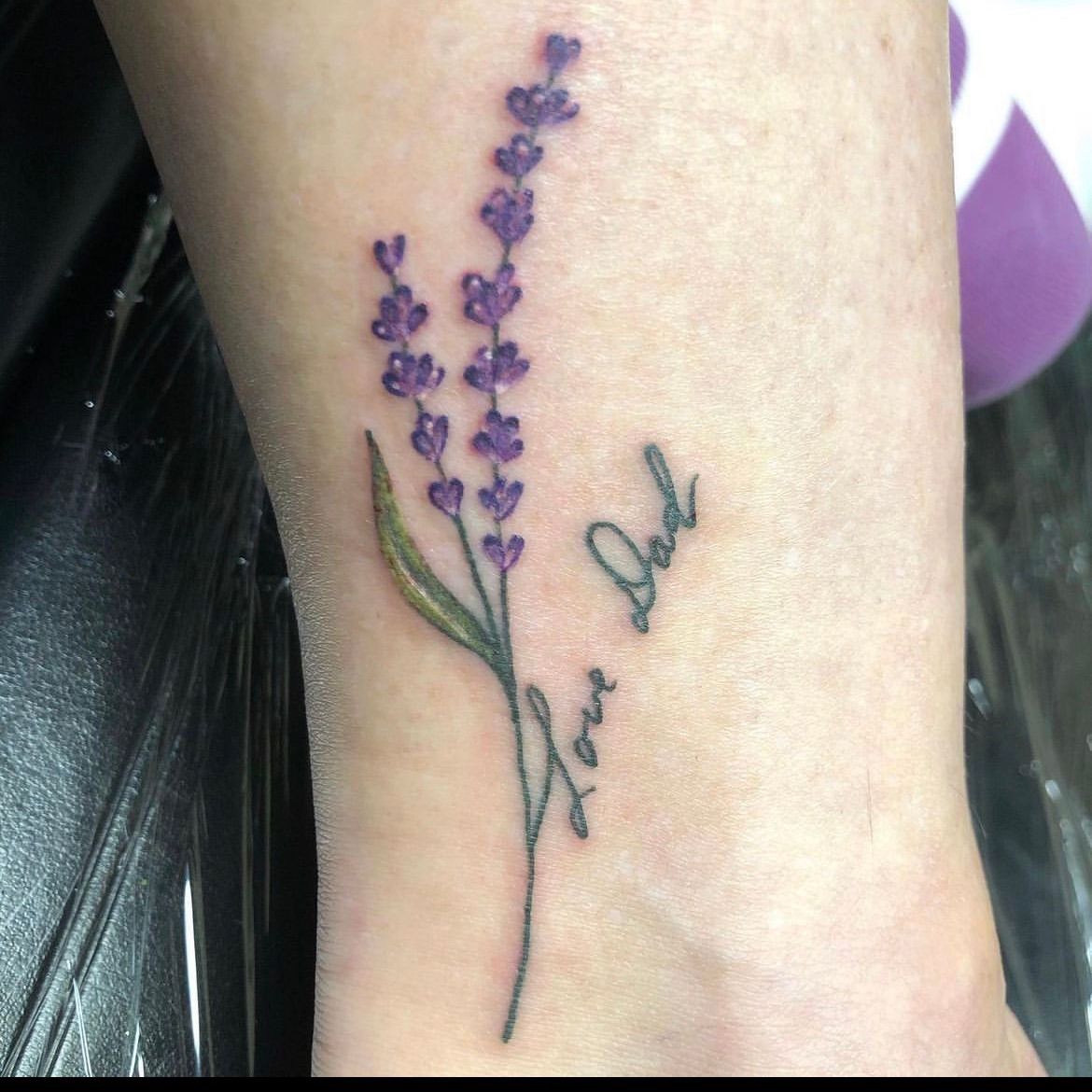 A woman has a tattoo of a lavender flower and the words love dad