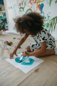A young girl is sitting on the floor painting a picture.
