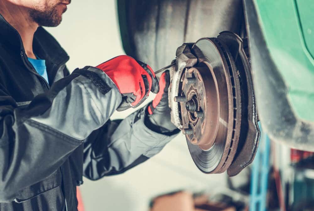 A Man Is Fixing A Brake Disc On A Car In A Garage — Matthew Harding Mechanical Repairs In Urunga, NSW