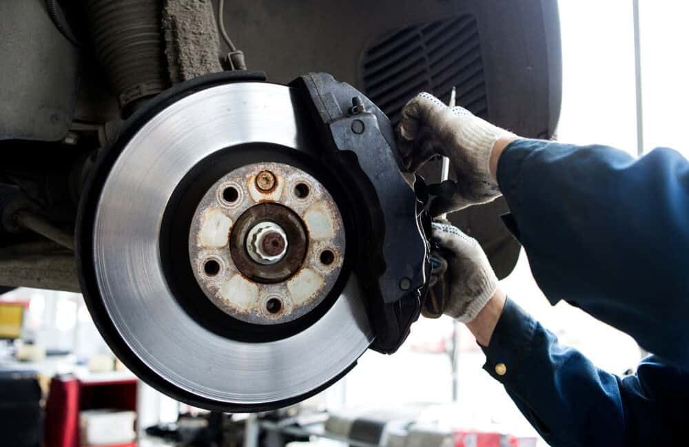A Man Is Fixing A Brake Disc On A Car In A Garage — Matthew Harding Mechanical Repairs In Urunga, NSW