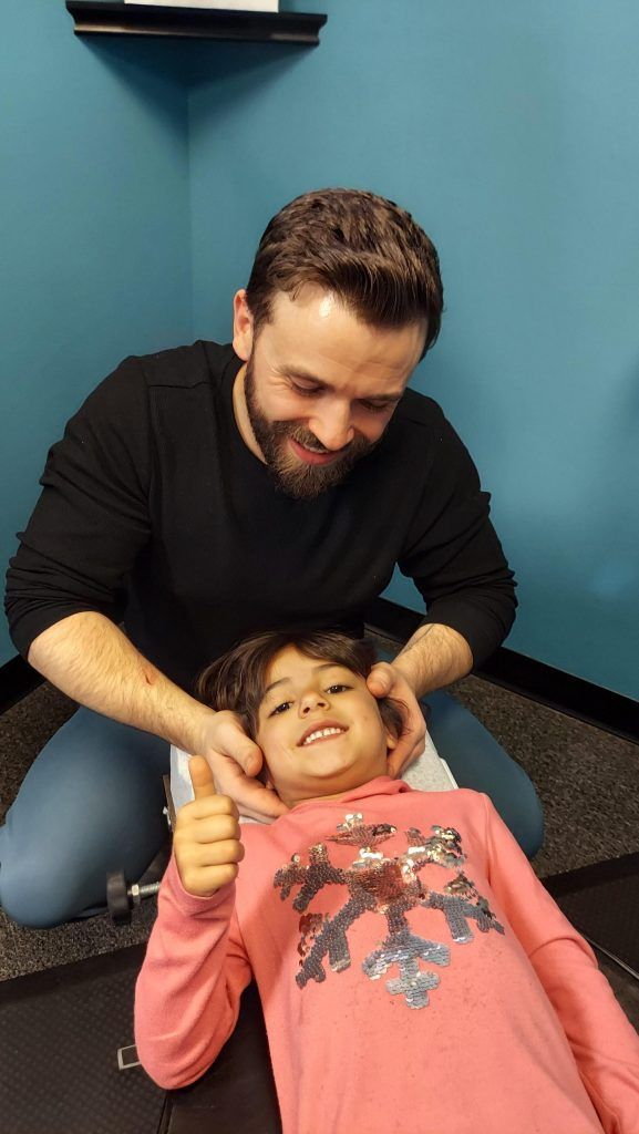 a little girl in a pink shirt is giving a thumbs up getting adjusted by chiropractor Dr. Nic