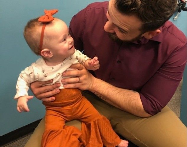 a Chiropractor is holding a baby with a bow on her head