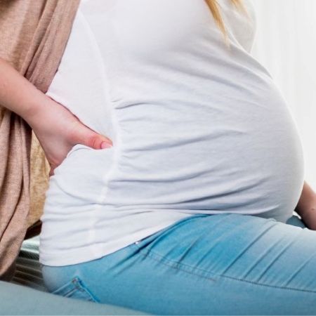 a pregnant woman is sitting down with her hand on her belly, back pain