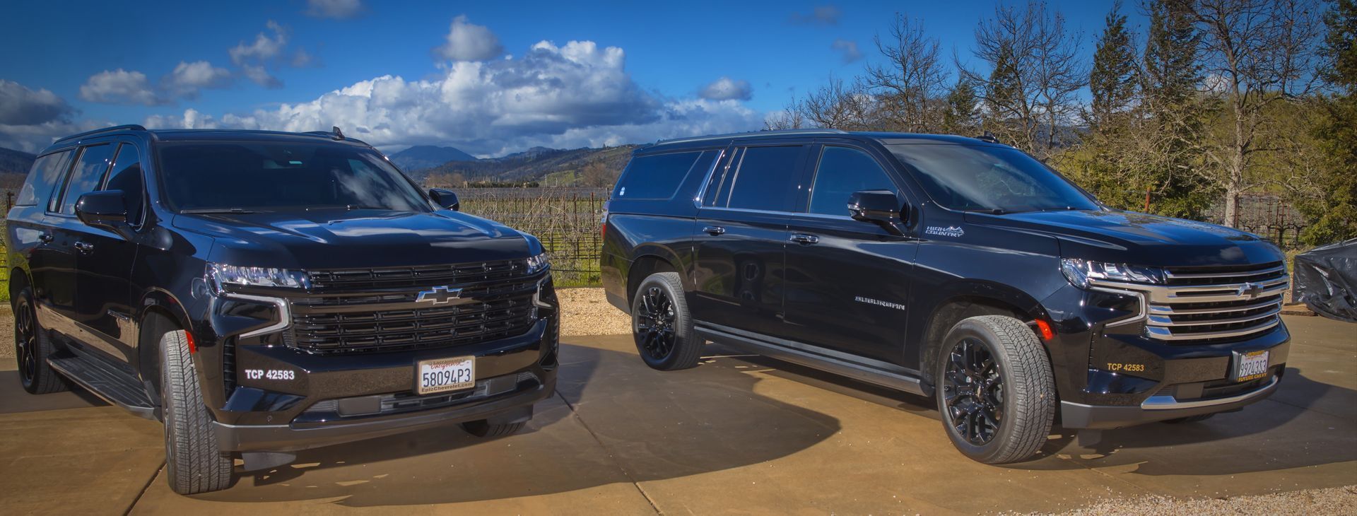 Two black suvs are parked next to each other on a dirt road.