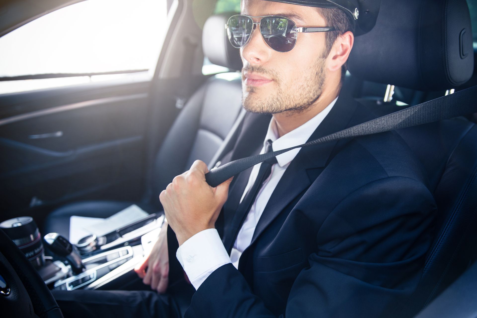 A man in a suit and tie is sitting in the driver's seat of a car.