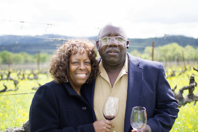 A man and a woman are standing next to each other in a field holding glasses of wine.