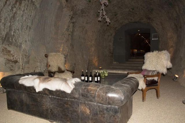 A living room with a couch , chairs and bottles of wine on a table.