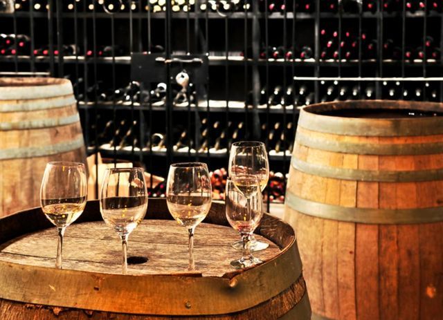 Four wine glasses are sitting on a wooden barrel in a wine cellar.