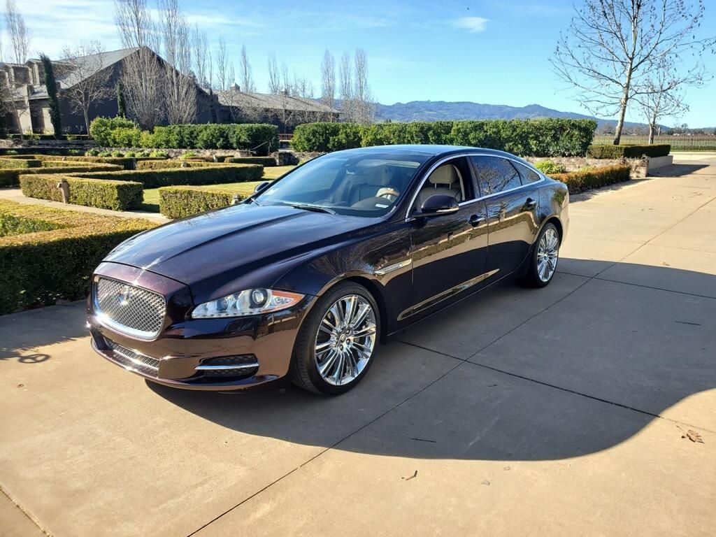 A black car is parked in a driveway in front of a hedge maze.