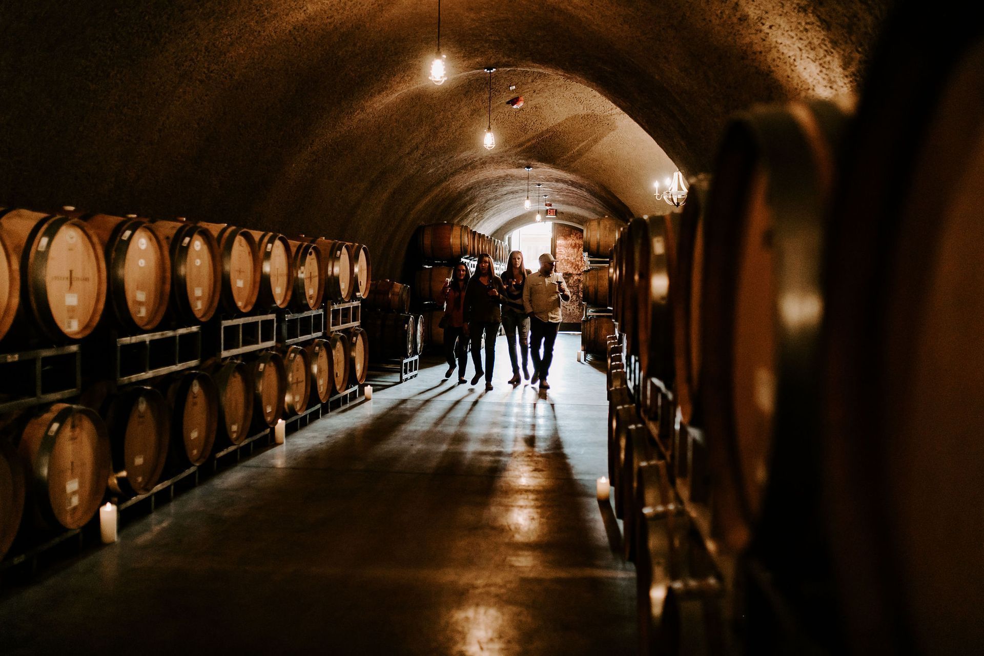 A group of people are walking through a wine cellar filled with barrels.