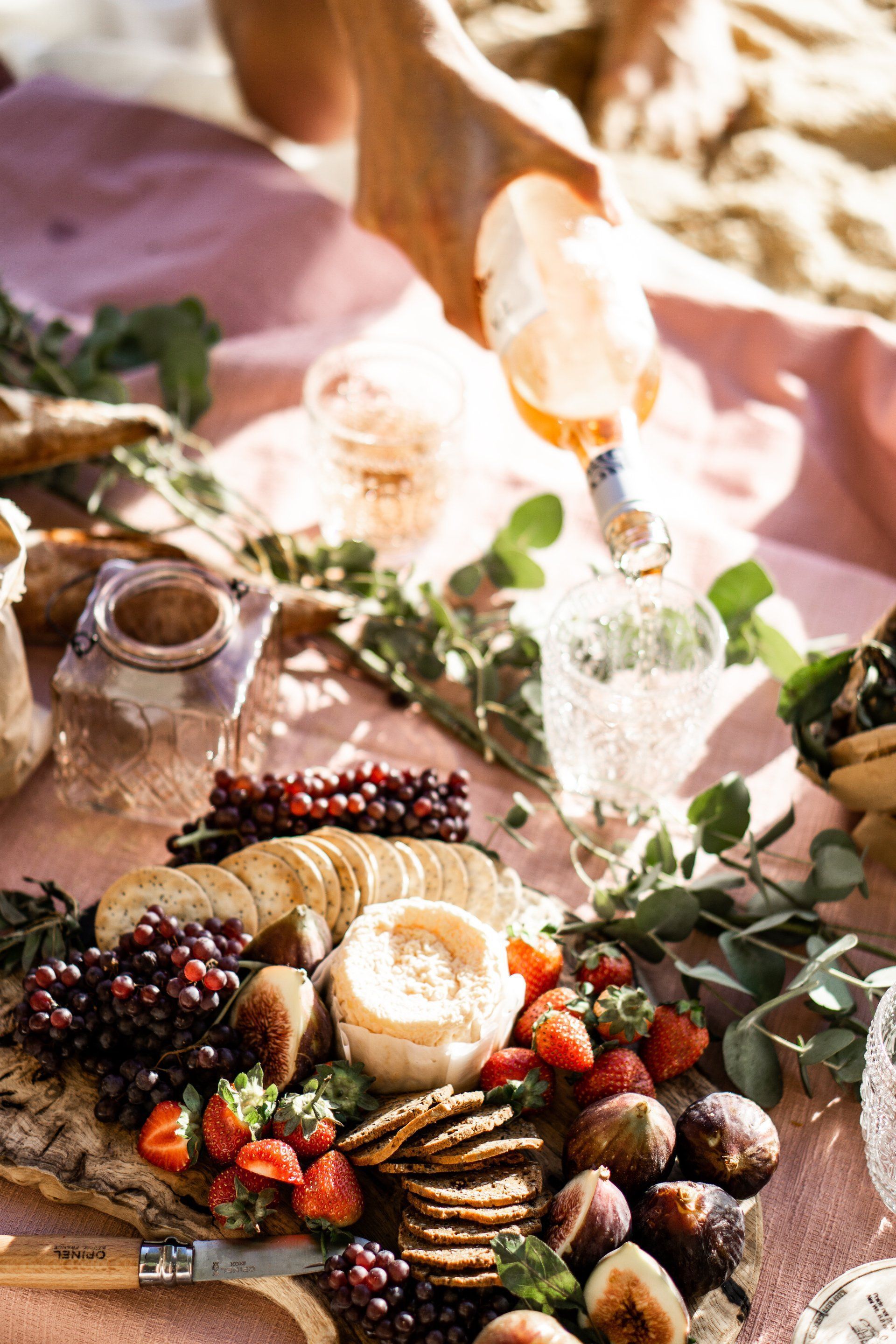 A person is pouring wine into a glass on a picnic table.