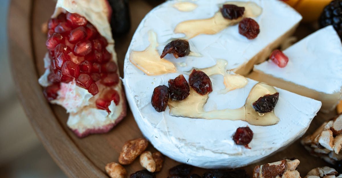 A piece of cheese is sitting on a wooden cutting board with nuts and fruit.