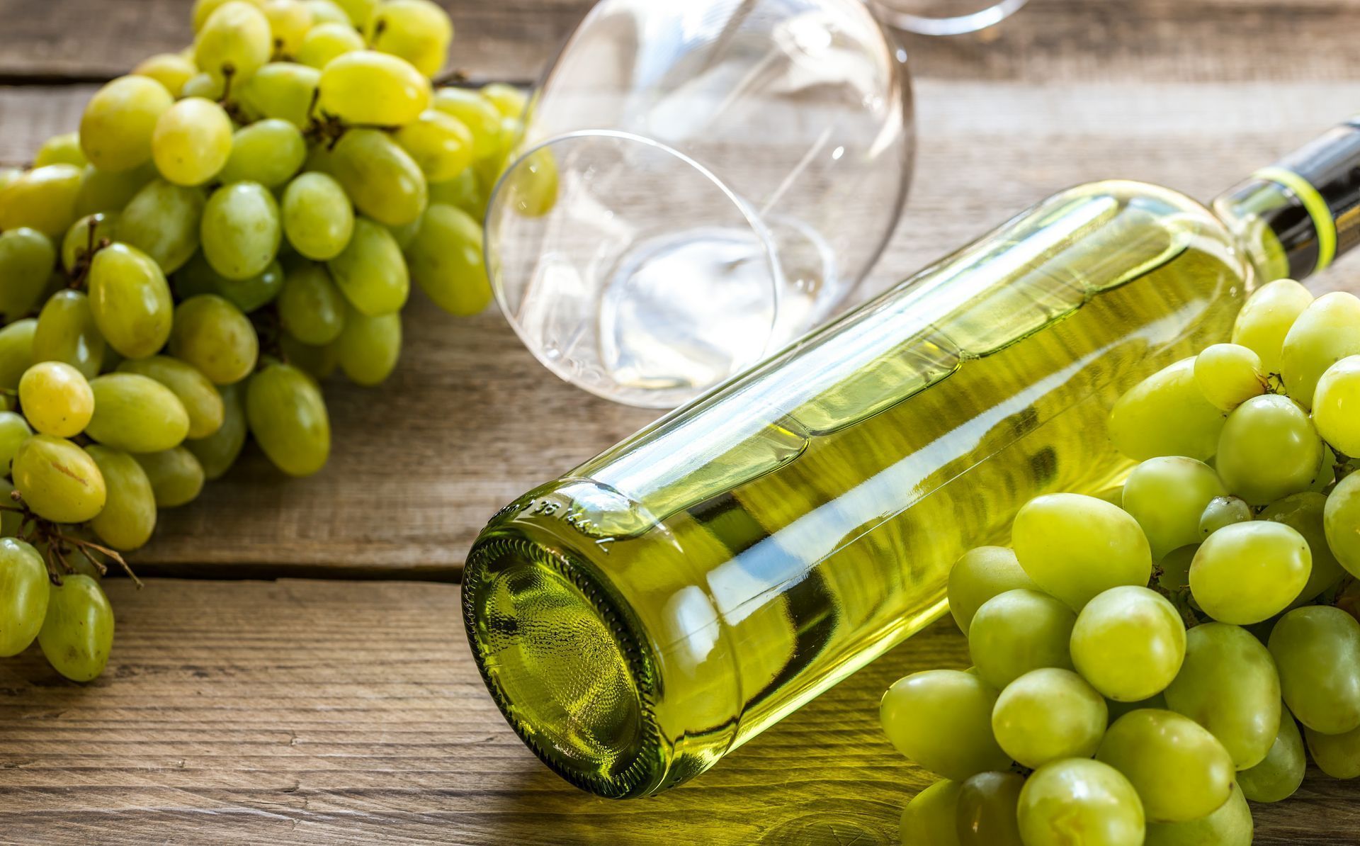 A bottle of white wine and a bunch of green grapes on a wooden table.