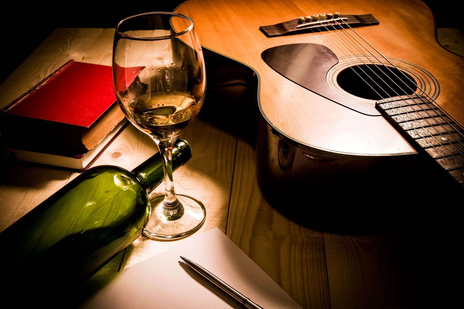 A bottle of wine a glass of wine and a guitar on a table.