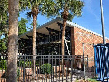 Building with brick facade, glass windows, and black metal fence, with palm trees in the foreground.