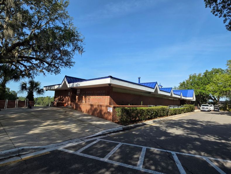Brick building with blue roof trim under a blue sky, trees surrounding.