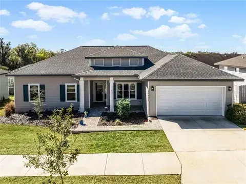 Gray single-story house with a white garage door, on a green lawn, under a blue sky.