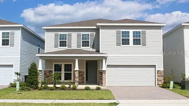 Two-story gray house with shutters and a stone facade, on a sunny day, with green lawn.