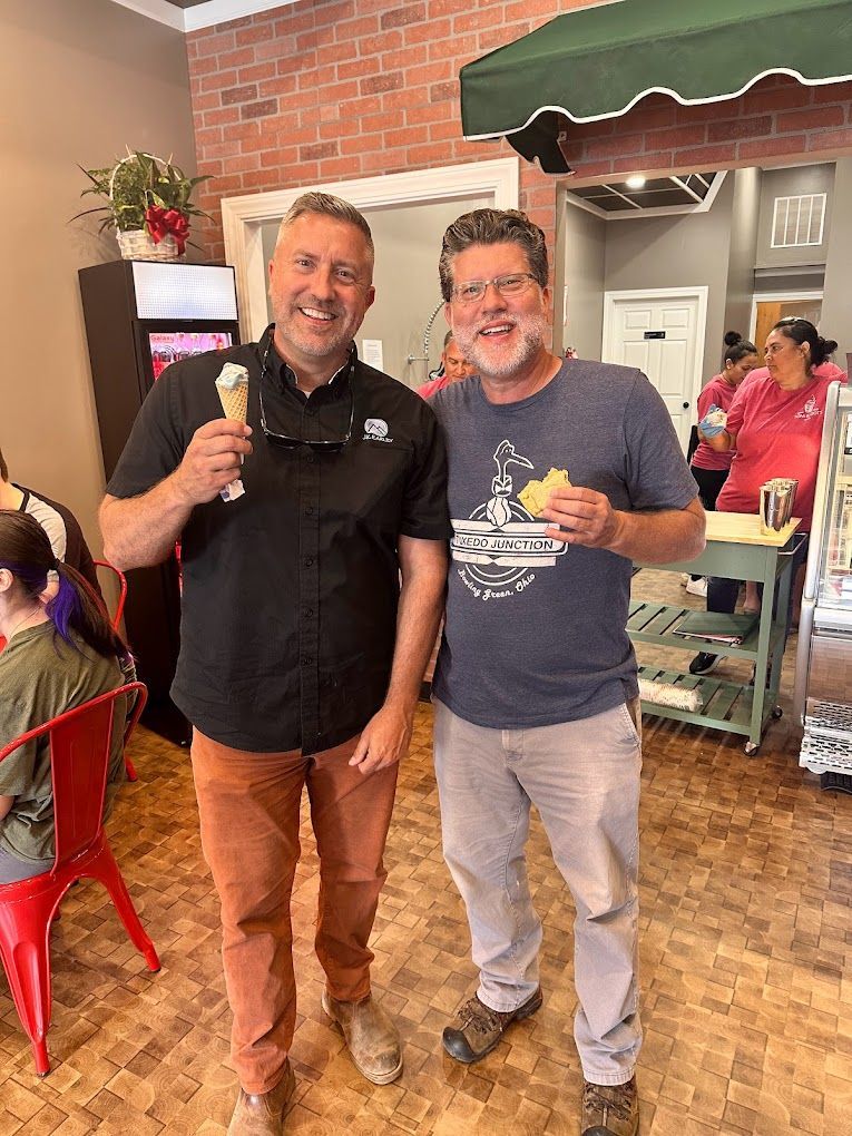 Two men are standing next to each other in a restaurant holding ice cream cones.