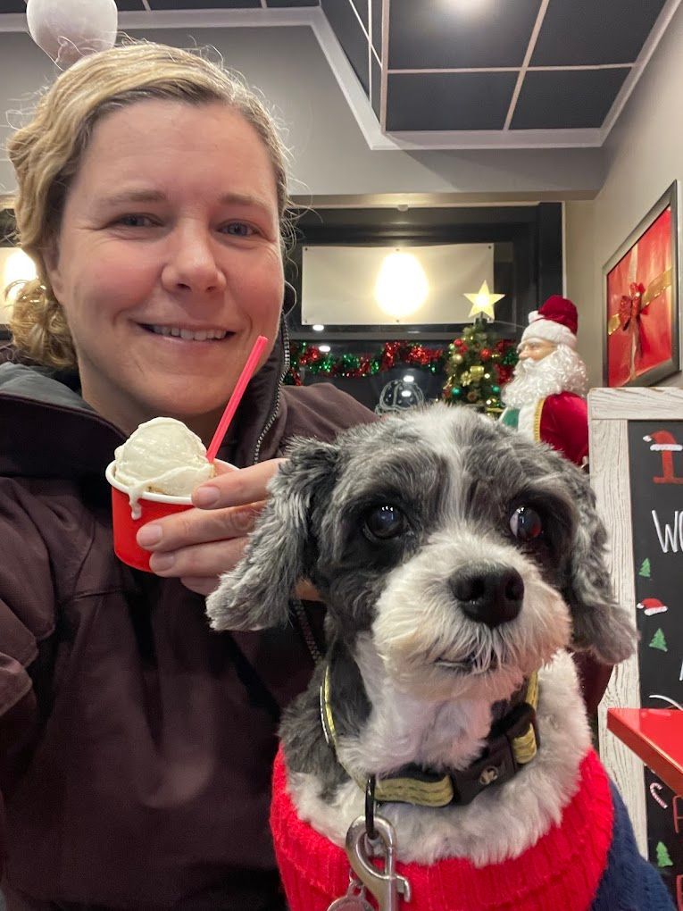 A woman is holding a cup of ice cream next to a small dog.
