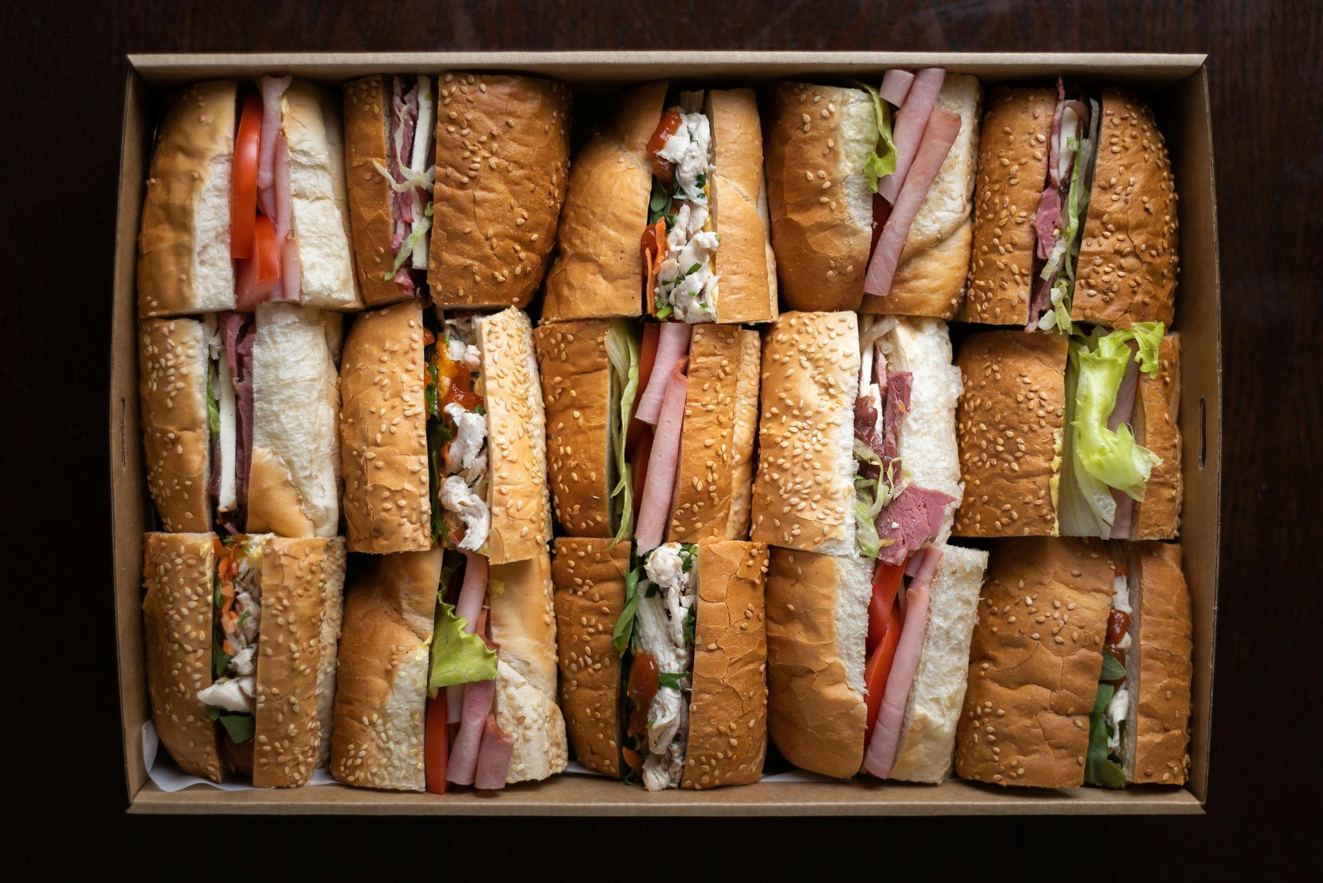 Box of assorted sandwiches on sesame seed baguettes, cut in half.