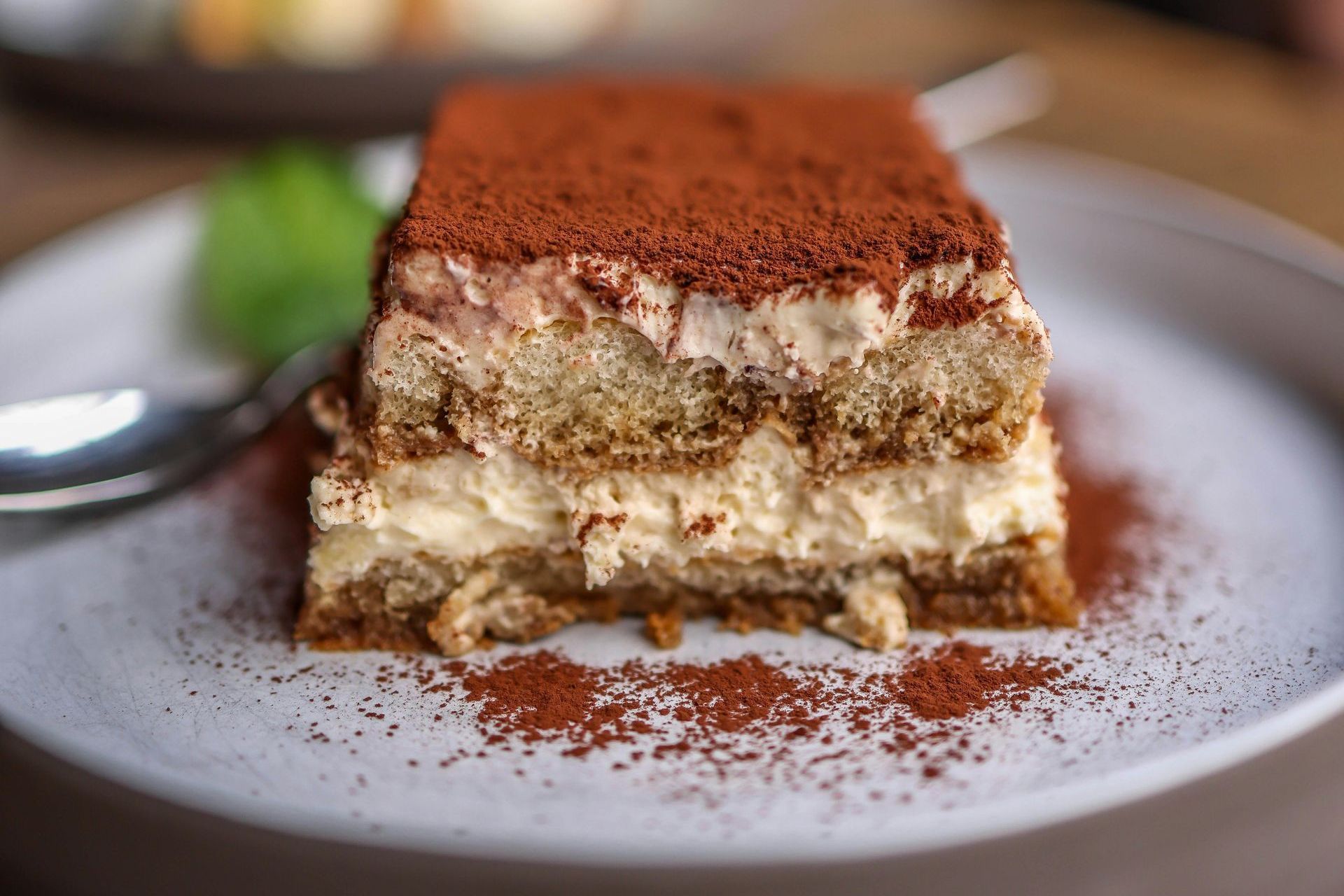 A close up of a piece of tiramisu on a plate with a spoon.