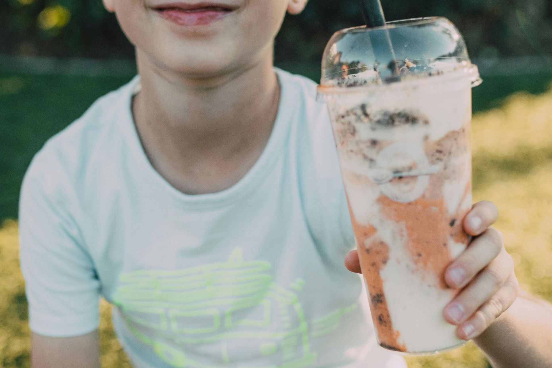 A young boy is holding a cup of milkshake with a straw.