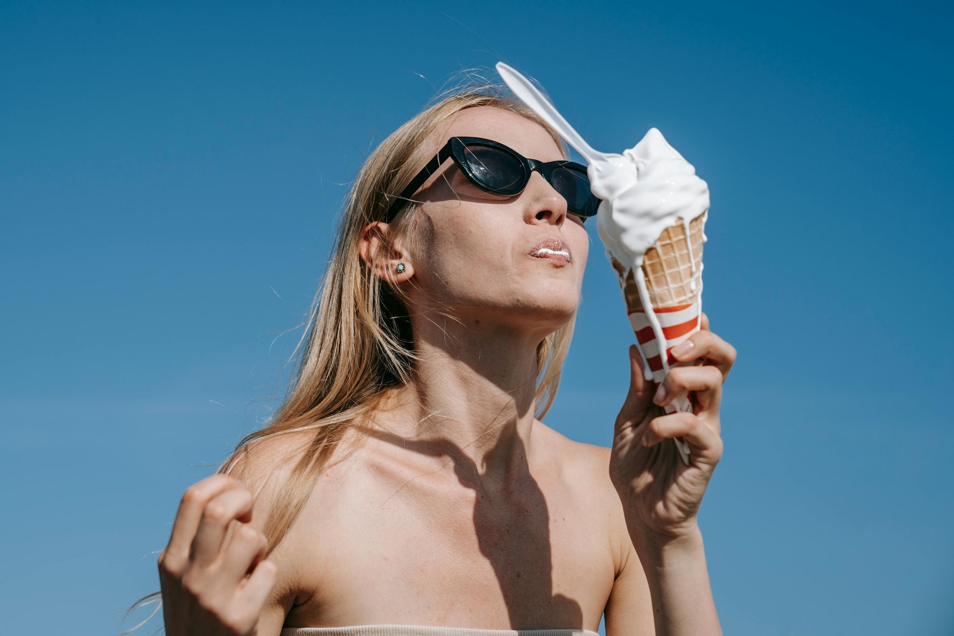 A woman is eating an ice cream cone with a spoon in her mouth.