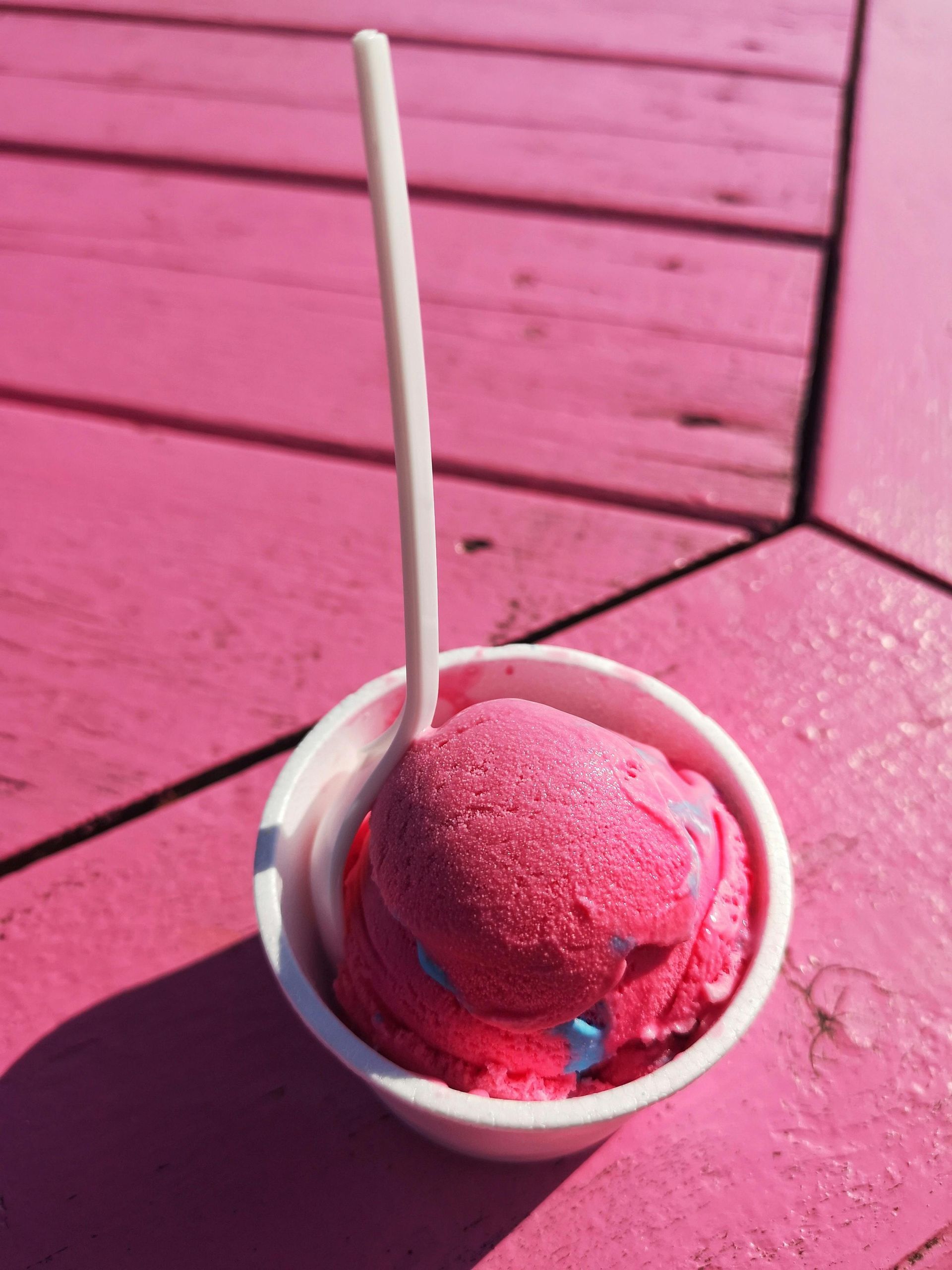 Pink Sorbetto in a white cup on a pink wooden surface with a white spoon.