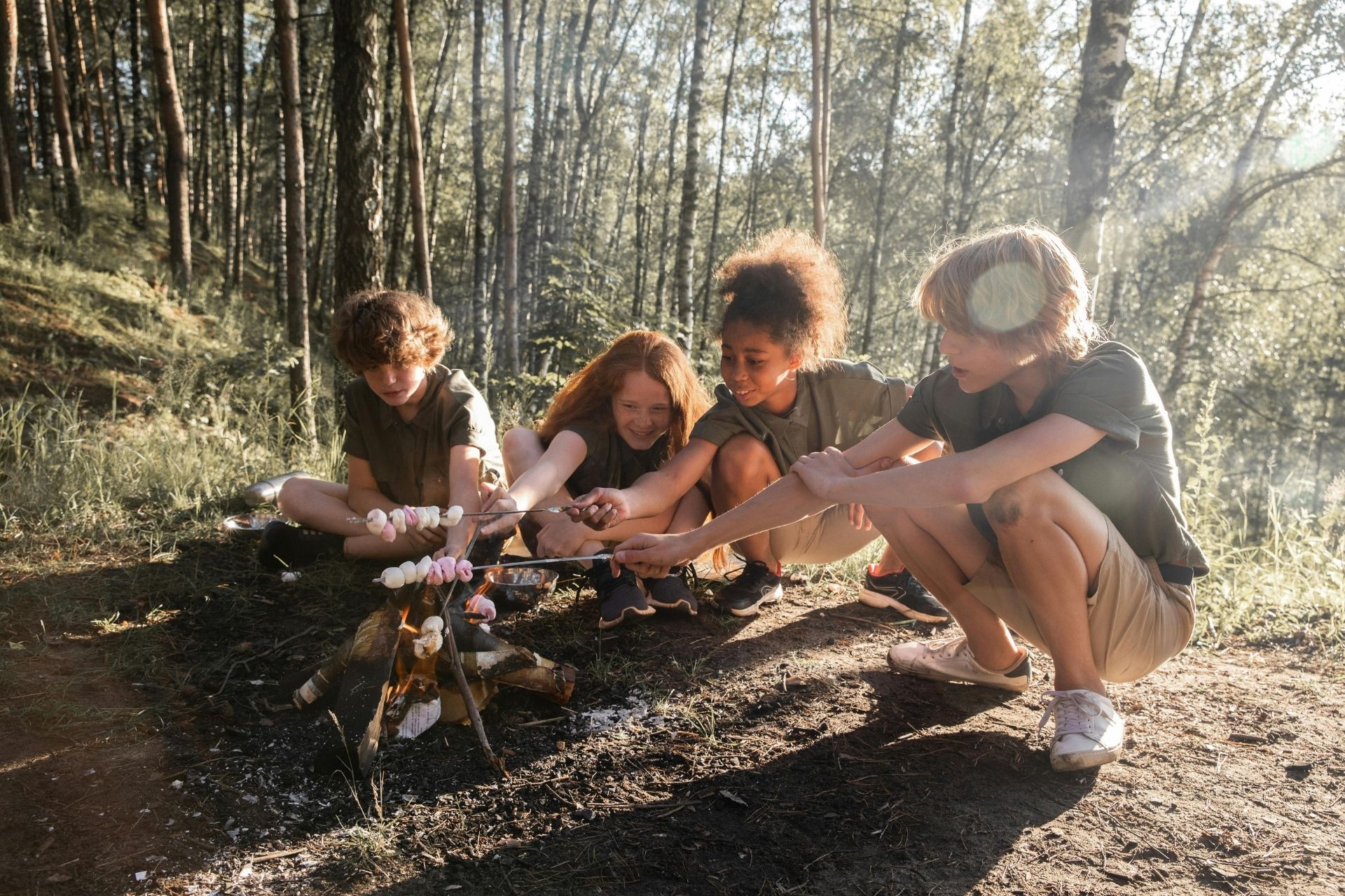 A group of children are sitting around a campfire in the woods.