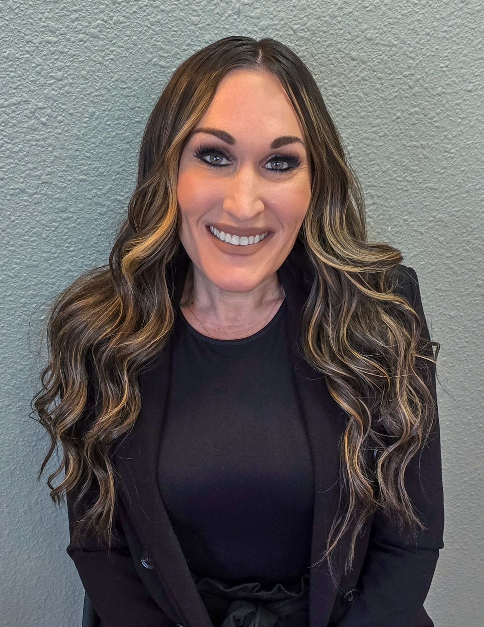 A woman with long hair is wearing a black jacket and smiling for the camera.