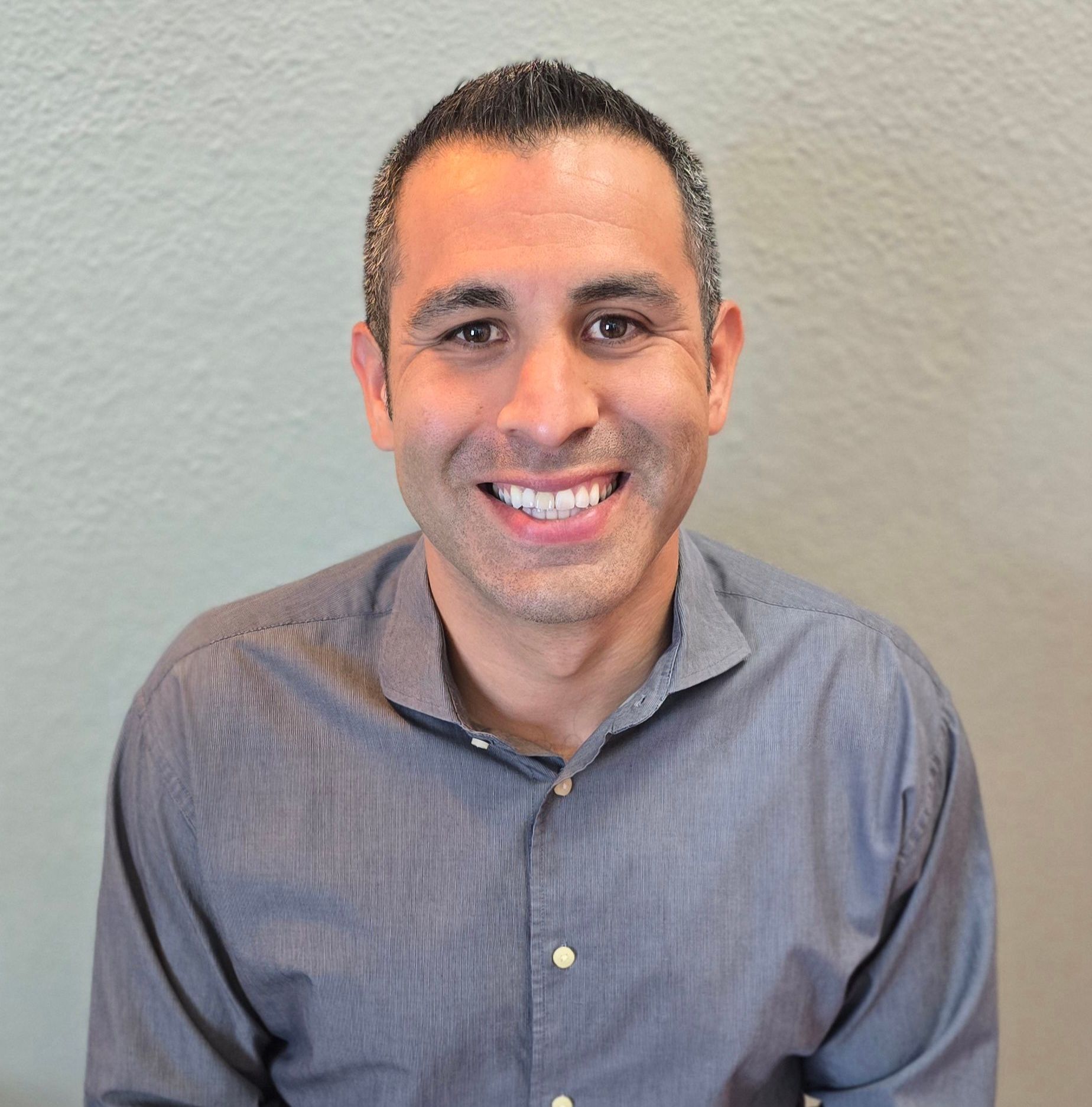 A man in a grey shirt is smiling for the camera