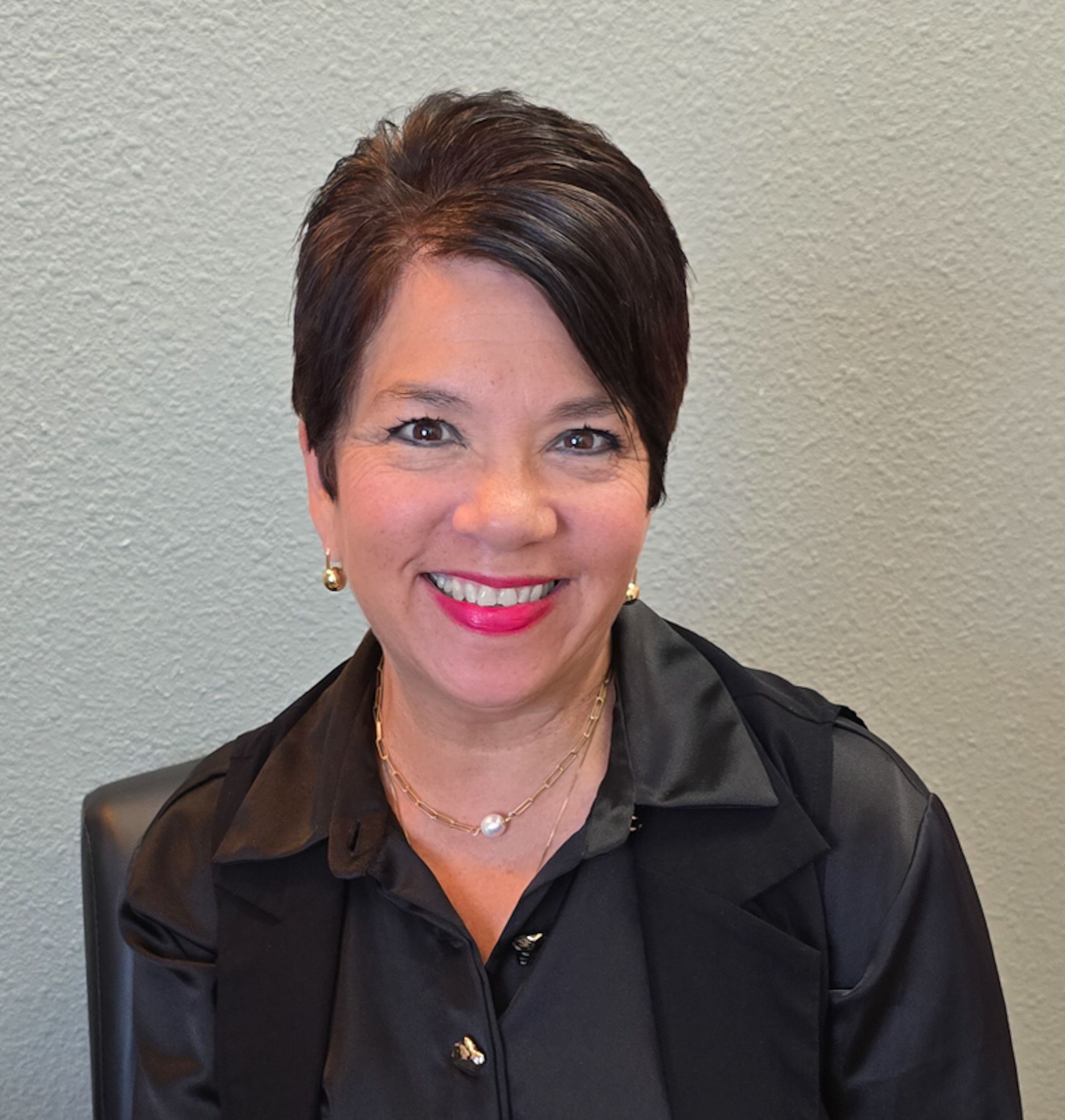 A woman wearing a black shirt and earrings is smiling for the camera.