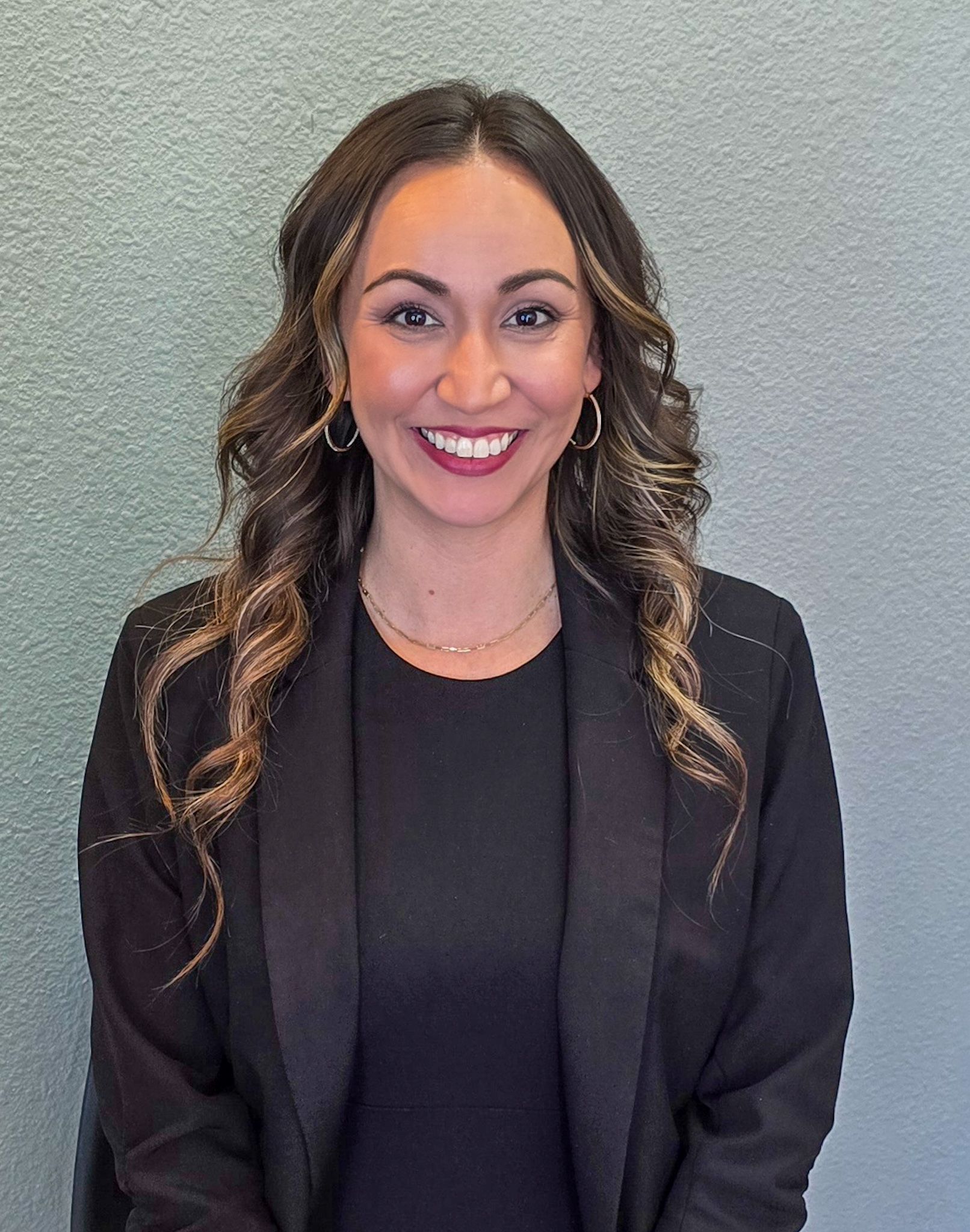A woman wearing a black jacket and a black shirt is smiling for the camera.