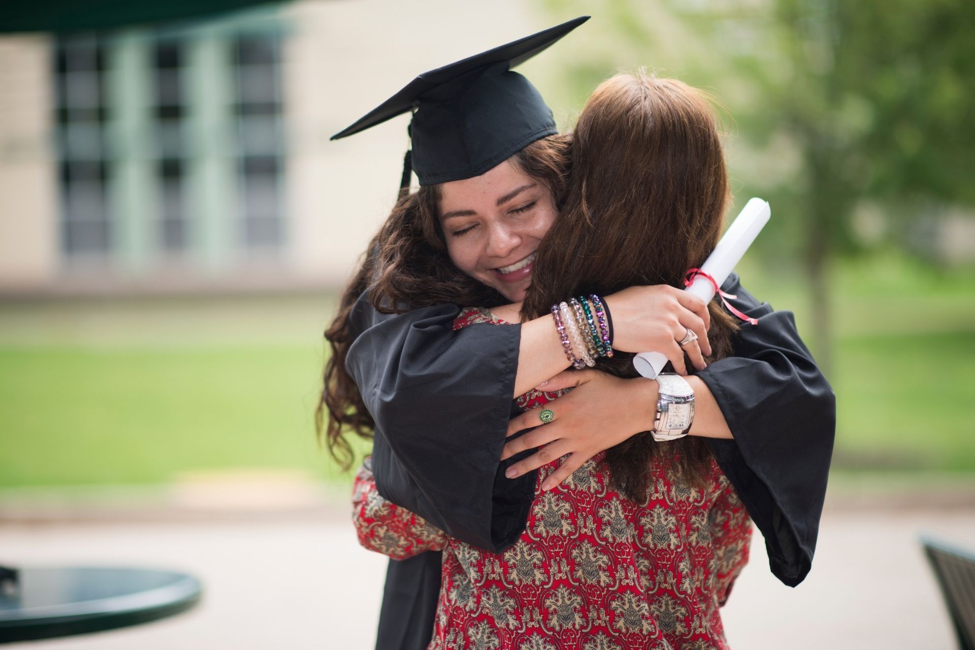 A woman in a graduation cap and gown is hugging another woman.